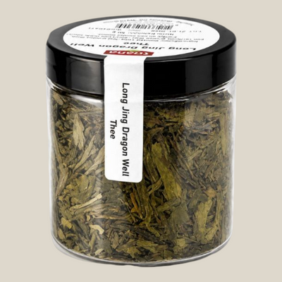 TuanaShop BV Long Jing Dragon Well groene thee in een transparante pot van 50 gram met een zwart deksel.