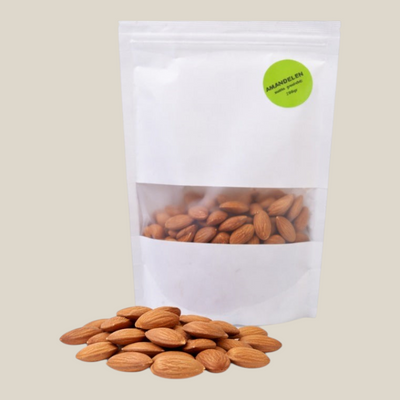 TuanaShop BV natuurlijke amandelen in een witte stazak van 200 gram met een hoopje ongebrande amandelen ervoor.
