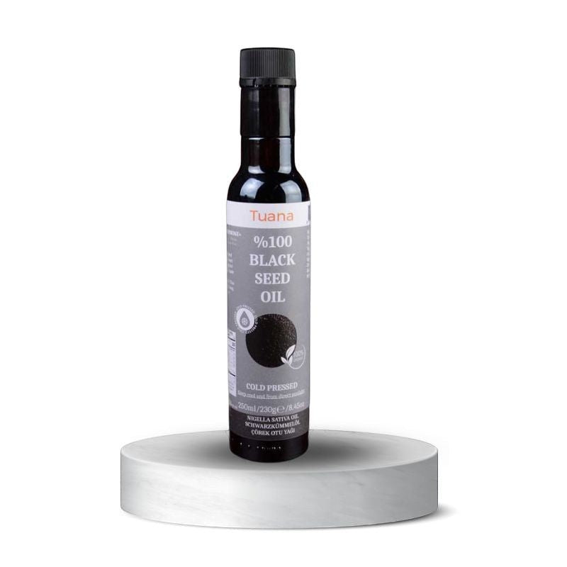 TuanaShop BV 100% biologische koudgeperste zwarte komijnzaadolie in een glazen fles van 250ml op een wit voetstuk.